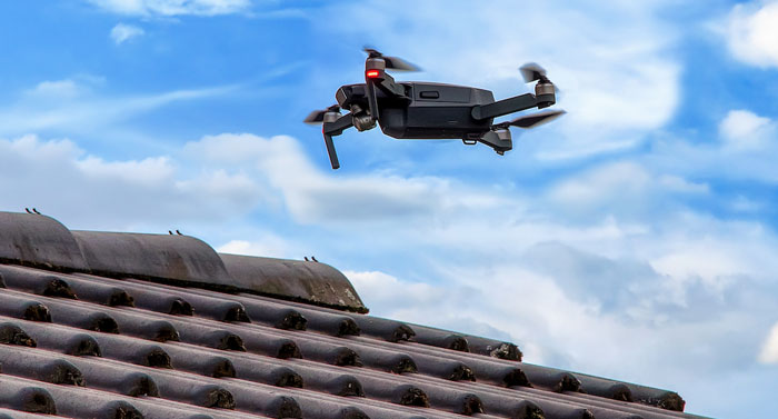 یک کوادکوپتر در حال پرواز در آسمان آبی و تصویر برداری از سقف یک خانه