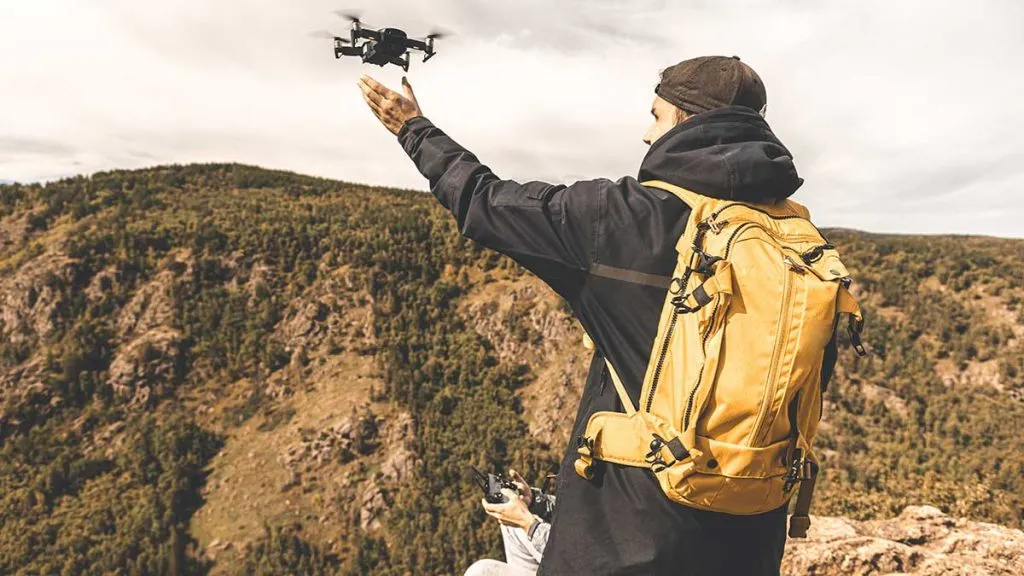 یک پسر روی قله کوه ایستاده و سعی دارد کوادکوپتر خود را پرواز دهد