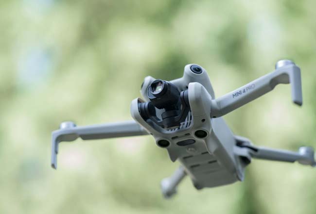 کوادکوپتر mini 4 pro ساخت dji در حال پرواز در یک جنگل و شاخ و برگ درختان در زمینه قرار دارند